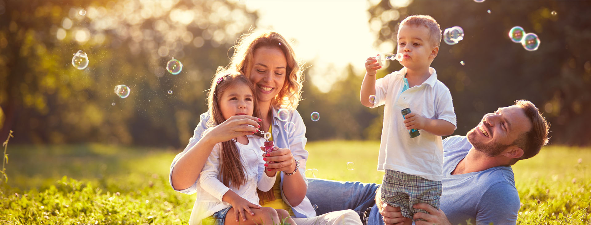A family of four sits on grass in a sunny park - pintlerinsurance.com