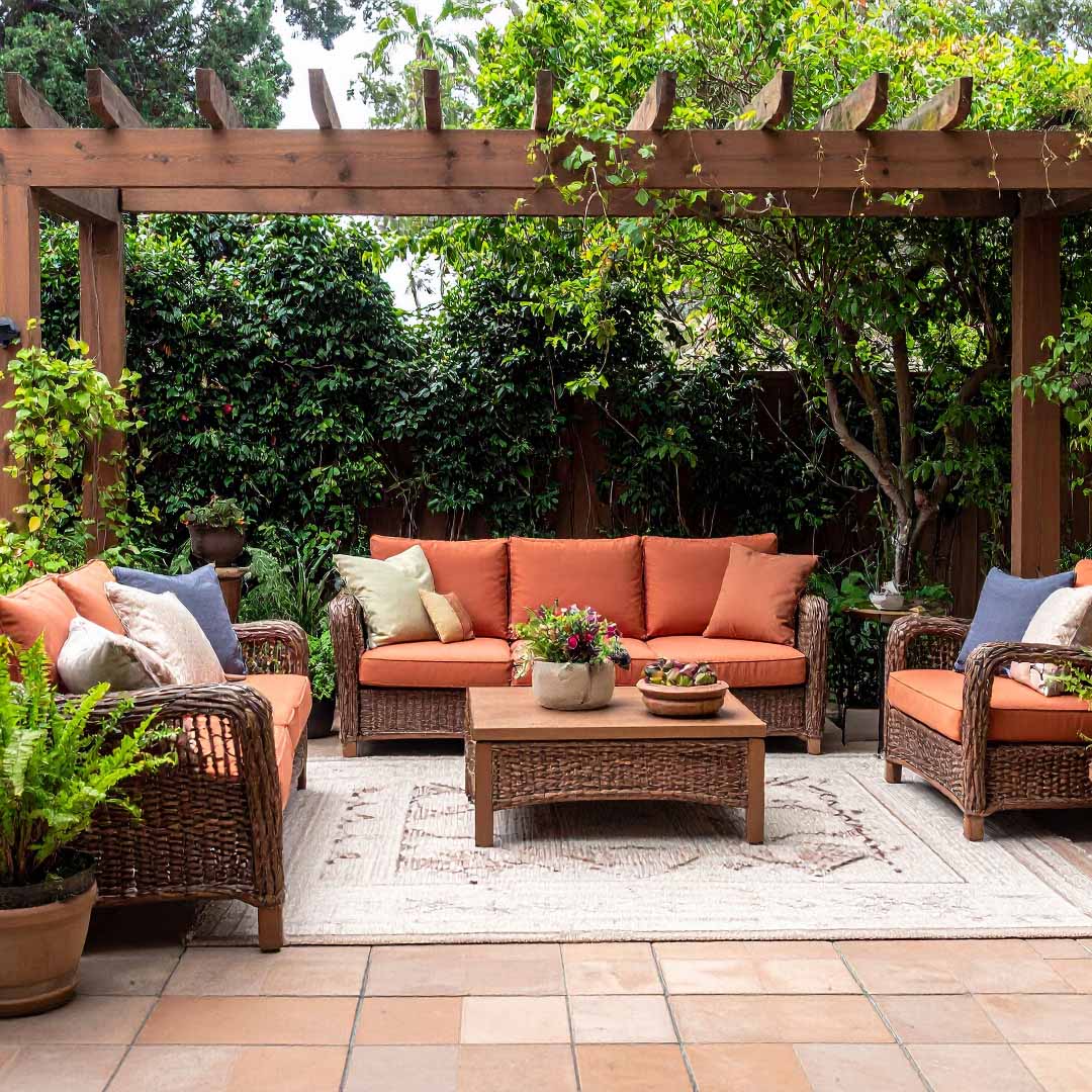 A cozy patio featuring wicker furniture surrounded by lush green plants, creating a serene outdoor space A cozy patio featuring wicker furniture surrounded by lush green plants, creating a serene outdoor space